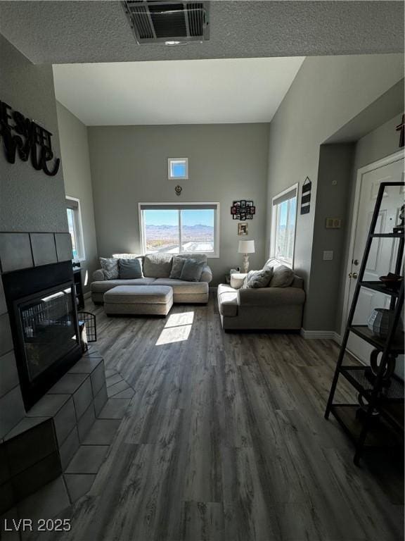 living room featuring a tile fireplace, wood-type flooring, plenty of natural light, and a towering ceiling