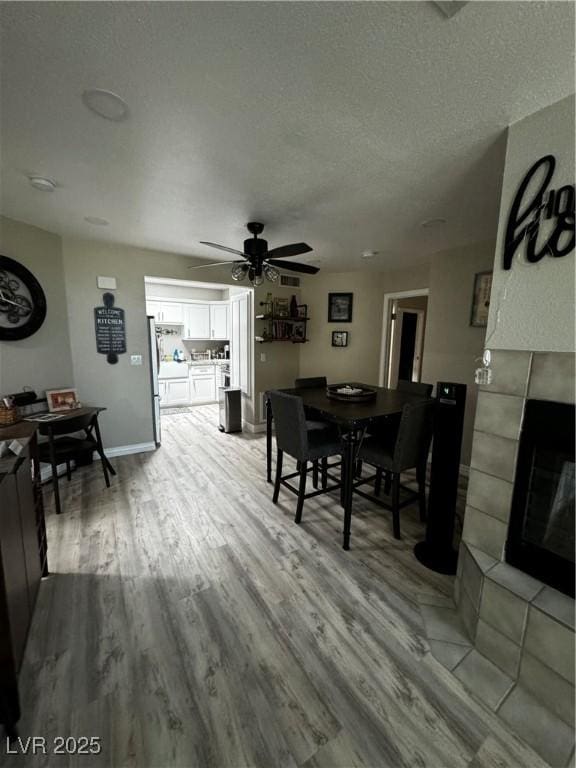 dining room with a tiled fireplace, ceiling fan, a textured ceiling, and light hardwood / wood-style floors