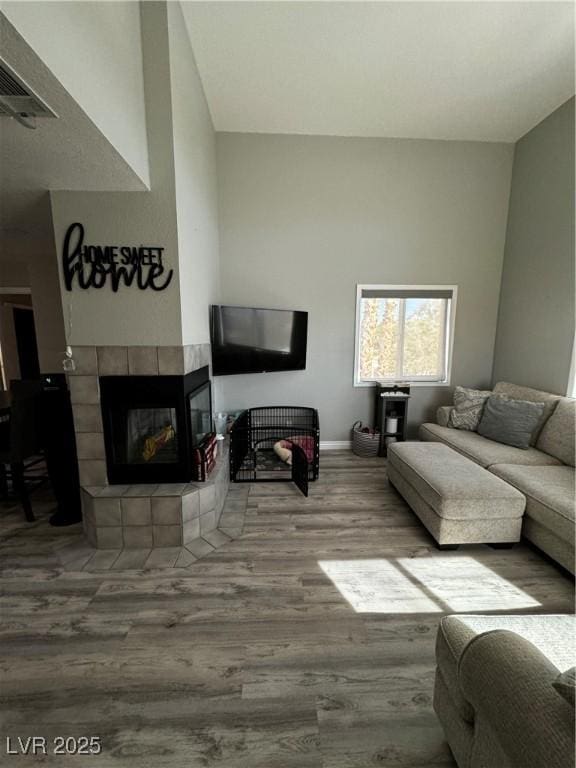 living room featuring wood-type flooring, a tile fireplace, and a high ceiling