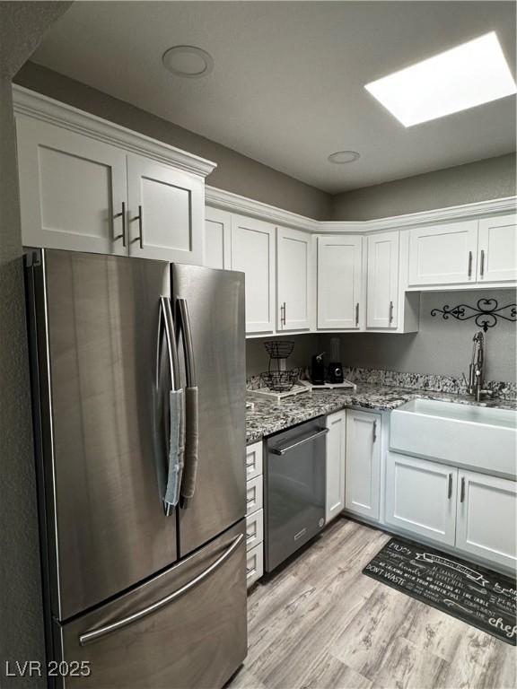 kitchen featuring white cabinetry, dishwashing machine, stainless steel fridge, light stone counters, and light wood-type flooring