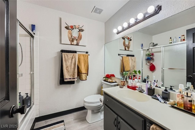 full bathroom with vanity, hardwood / wood-style floors, bath / shower combo with glass door, and toilet