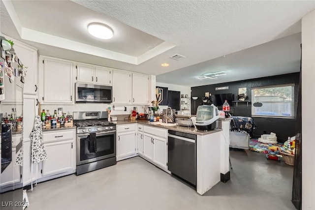 kitchen with a textured ceiling, kitchen peninsula, a raised ceiling, stainless steel appliances, and white cabinets