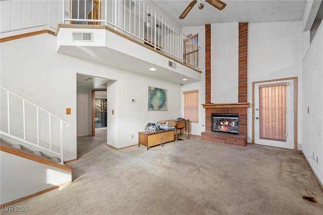 unfurnished living room featuring a high ceiling, ceiling fan, carpet, and a fireplace