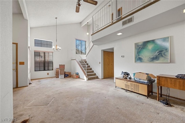 carpeted living room with ceiling fan with notable chandelier, high vaulted ceiling, and a textured ceiling