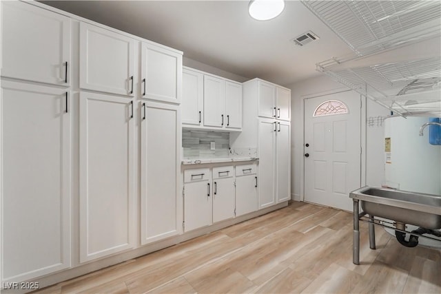 kitchen with white cabinetry, backsplash, and light hardwood / wood-style flooring