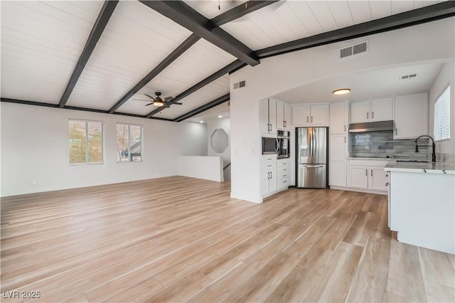 kitchen featuring lofted ceiling with beams, white cabinetry, sink, and stainless steel fridge