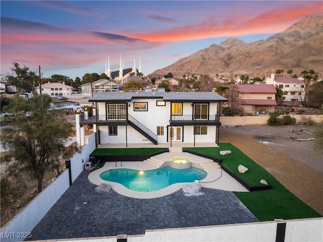 back house at dusk with a balcony, a mountain view, a pool with hot tub, and a patio area