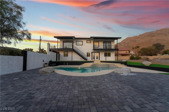 back house at dusk featuring a fenced in pool, a balcony, a mountain view, and a patio area