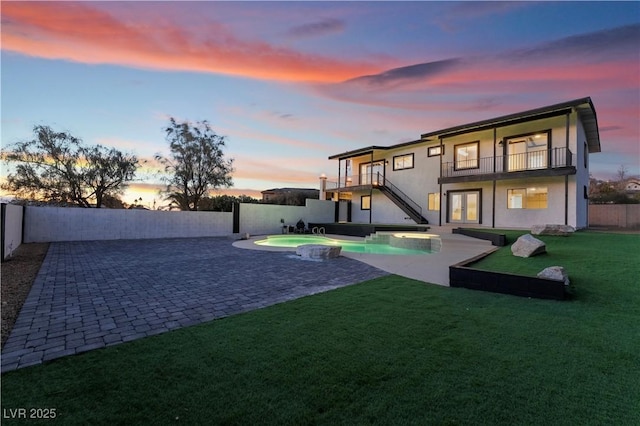 back house at dusk featuring a fenced in pool, a balcony, a yard, and a patio area