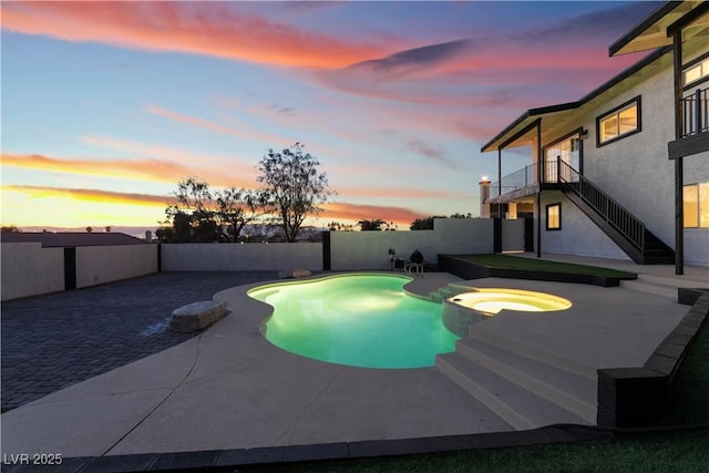 pool at dusk featuring a patio and an in ground hot tub