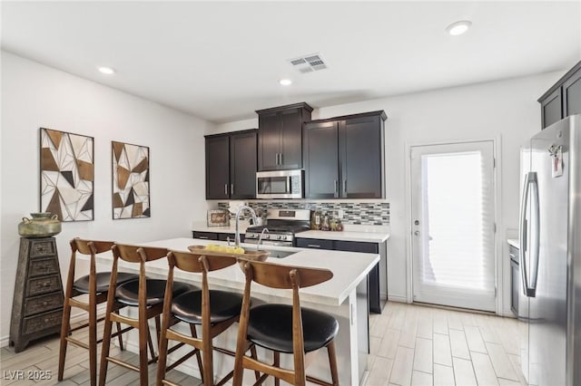 kitchen featuring appliances with stainless steel finishes, a breakfast bar, tasteful backsplash, sink, and a center island with sink