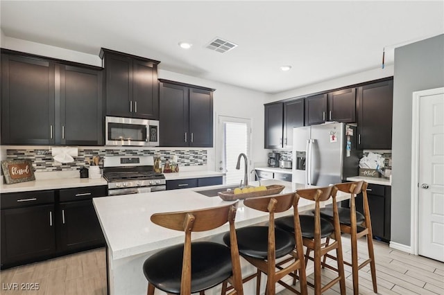 kitchen featuring a breakfast bar, sink, appliances with stainless steel finishes, a kitchen island with sink, and backsplash