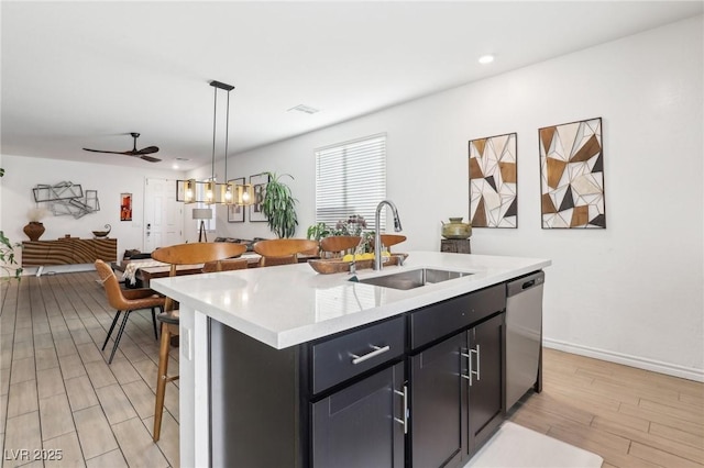 kitchen featuring a breakfast bar, decorative light fixtures, dishwasher, sink, and a kitchen island with sink