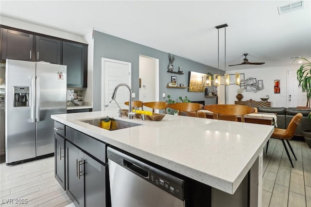 kitchen with sink, ceiling fan, stainless steel appliances, an island with sink, and decorative light fixtures