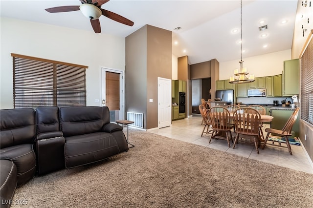 living room with visible vents, a towering ceiling, a ceiling fan, light carpet, and light tile patterned flooring