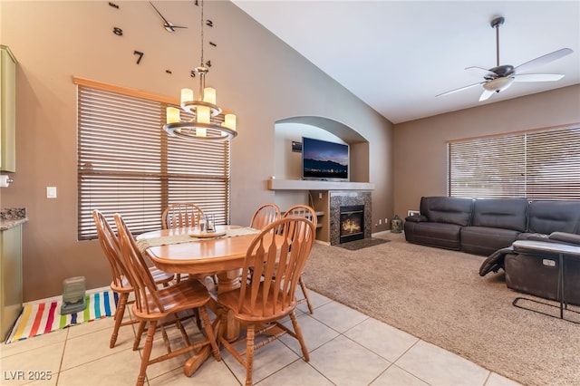 dining room with light carpet, ceiling fan with notable chandelier, a tiled fireplace, and light tile patterned flooring