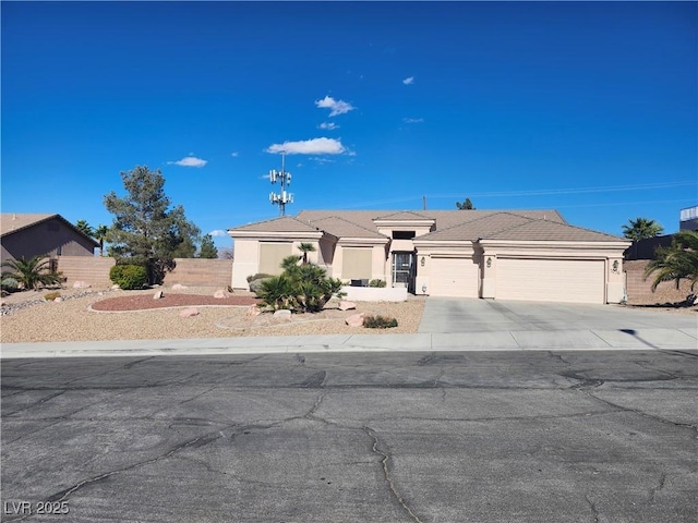 view of front of property featuring a tile roof, stucco siding, fence, a garage, and driveway