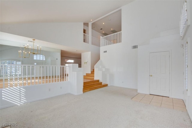 unfurnished living room with light carpet, high vaulted ceiling, and a chandelier