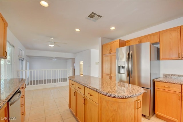 kitchen with ceiling fan, appliances with stainless steel finishes, a kitchen island, light stone countertops, and light tile patterned flooring