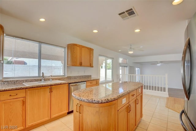 kitchen with sink, light tile patterned floors, appliances with stainless steel finishes, light stone countertops, and a kitchen island