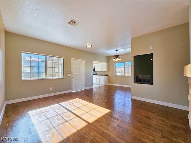 unfurnished living room featuring ceiling fan, dark wood finished floors, visible vents, and baseboards