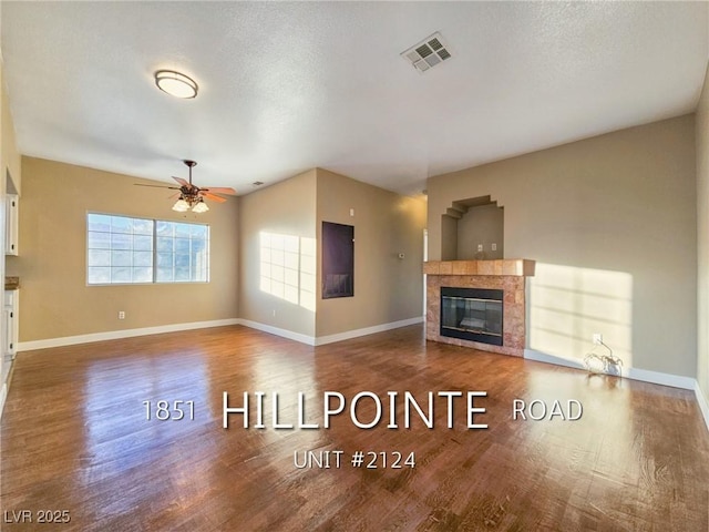 unfurnished living room featuring ceiling fan, a tile fireplace, wood finished floors, and visible vents