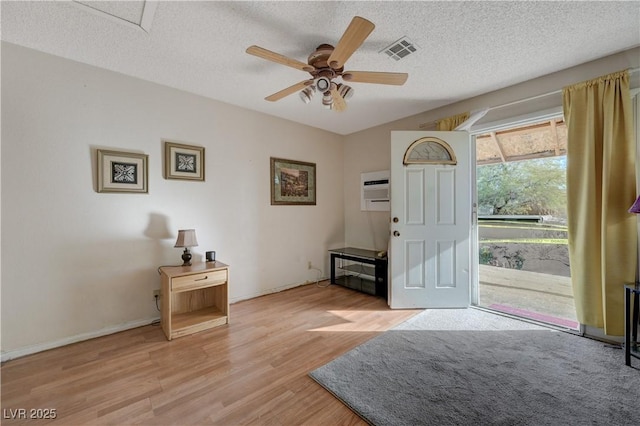 entryway featuring ceiling fan, a wall mounted air conditioner, a textured ceiling, and light hardwood / wood-style floors