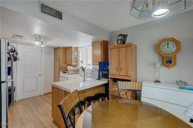 kitchen with tile countertops, stainless steel refrigerator, a textured ceiling, and light wood-type flooring