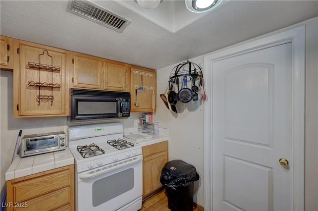 kitchen with light brown cabinetry, tile countertops, gas range gas stove, and a textured ceiling