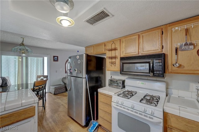 kitchen with white gas range, decorative light fixtures, tile countertops, and stainless steel refrigerator