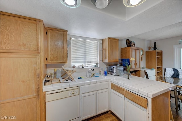 kitchen featuring white dishwasher, sink, tile counters, and kitchen peninsula