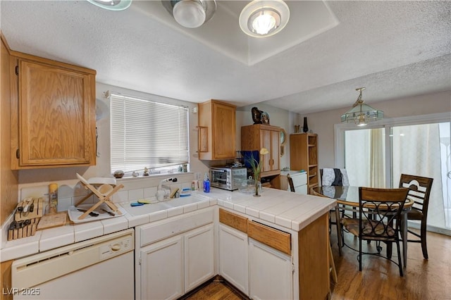 kitchen with pendant lighting, tile countertops, sink, white dishwasher, and kitchen peninsula