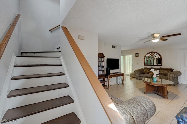 stairway with tile patterned flooring, ceiling fan, and a textured ceiling