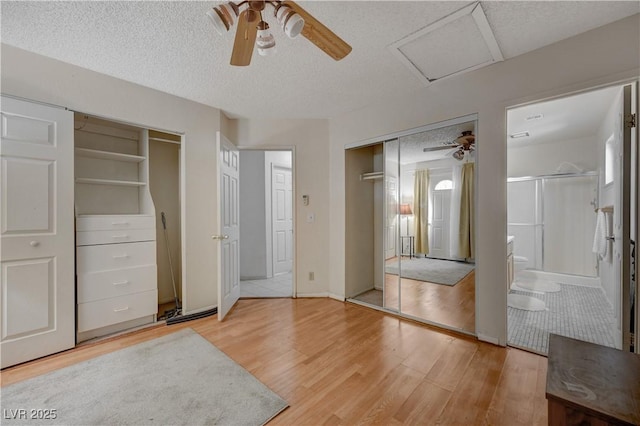 bedroom with ensuite bathroom, wood-type flooring, ceiling fan, multiple closets, and a textured ceiling