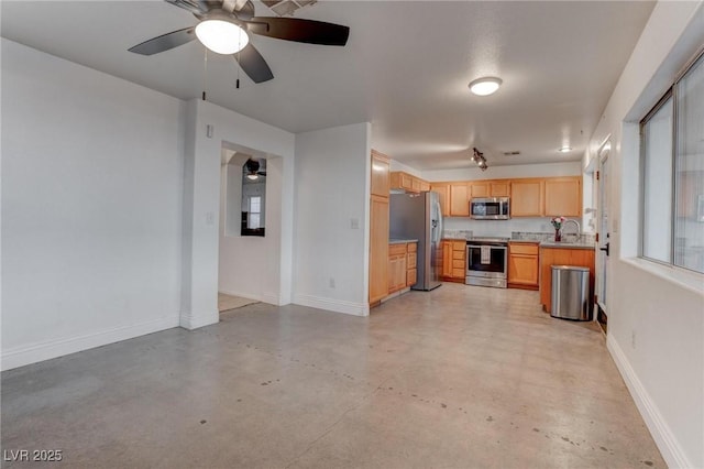 kitchen with appliances with stainless steel finishes, light brown cabinets, a sink, concrete floors, and baseboards