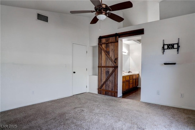 empty room with visible vents, a high ceiling, a barn door, a ceiling fan, and carpet flooring