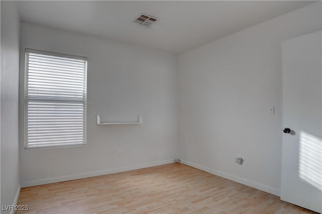 spare room featuring plenty of natural light, wood finished floors, visible vents, and baseboards