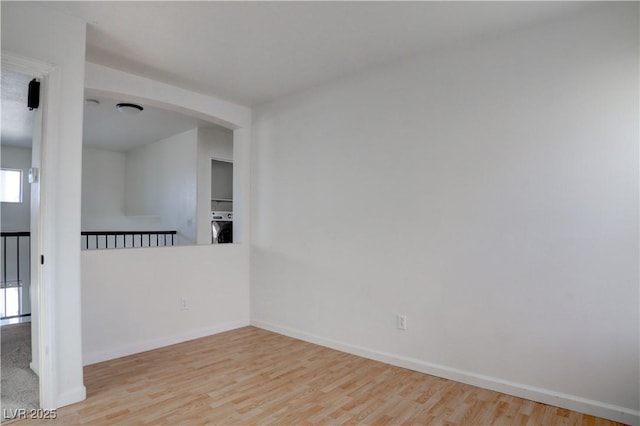 unfurnished room with baseboards, washer / clothes dryer, arched walkways, and wood finished floors