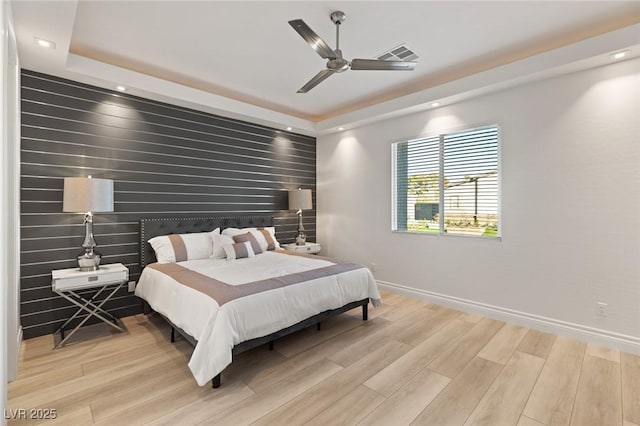 bedroom with ceiling fan, a raised ceiling, and light hardwood / wood-style floors