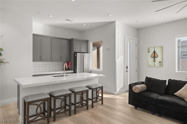 kitchen with sink, gray cabinets, stainless steel refrigerator, and a center island with sink