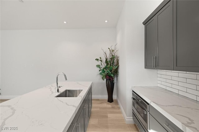 kitchen with light stone countertops, sink, gray cabinetry, and backsplash