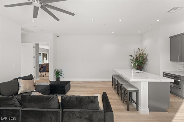 living room with ceiling fan, sink, and light hardwood / wood-style floors