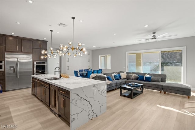 kitchen featuring sink, appliances with stainless steel finishes, hanging light fixtures, light stone countertops, and a center island with sink