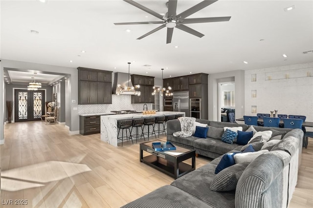 living room with ceiling fan with notable chandelier, sink, light hardwood / wood-style flooring, and french doors