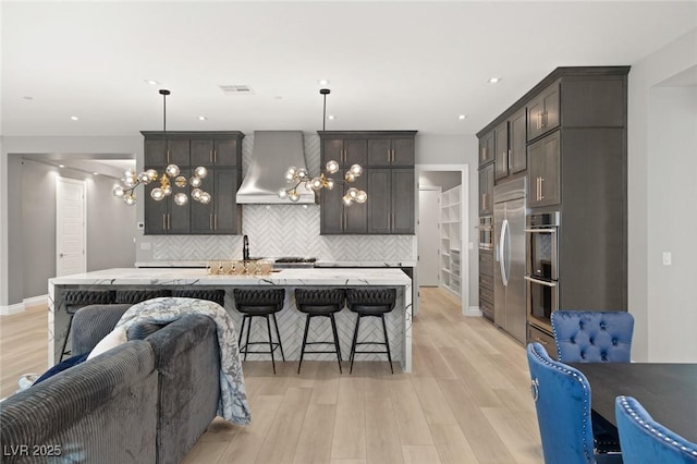 kitchen with pendant lighting, wall chimney exhaust hood, an island with sink, and tasteful backsplash