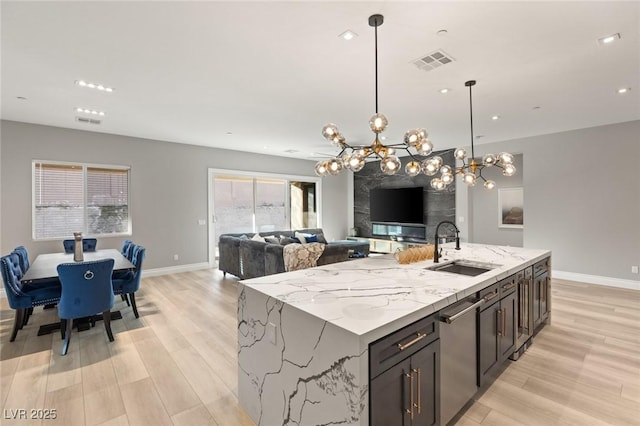 kitchen featuring pendant lighting, sink, light stone countertops, a center island with sink, and light wood-type flooring