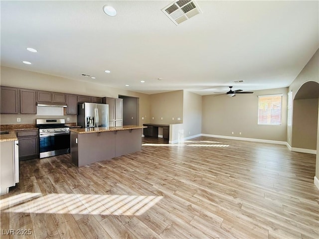 kitchen featuring a center island, appliances with stainless steel finishes, ceiling fan, light stone countertops, and light hardwood / wood-style floors