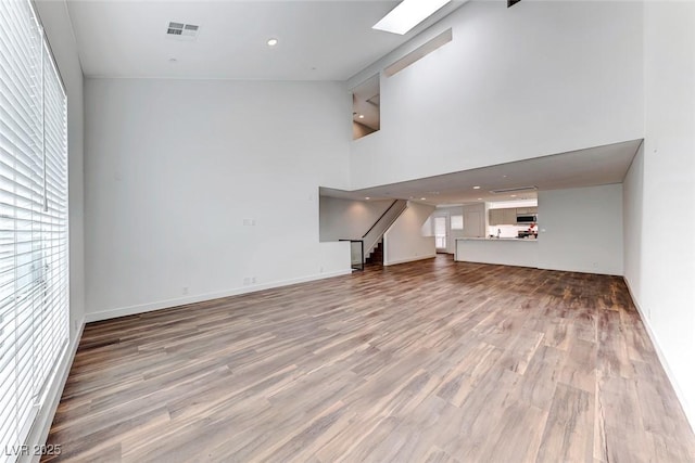 unfurnished living room with hardwood / wood-style flooring, a towering ceiling, and a skylight