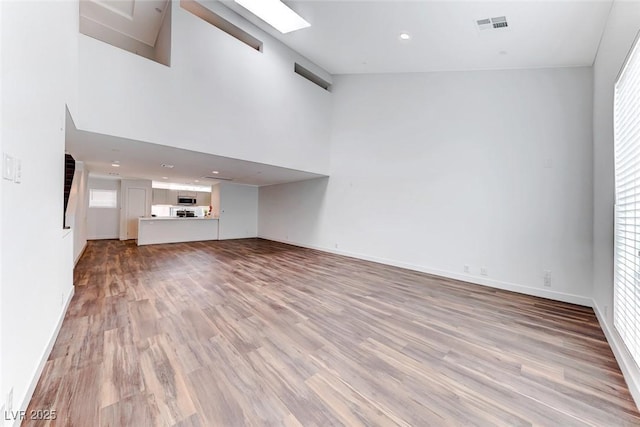 unfurnished living room featuring a towering ceiling and light hardwood / wood-style floors