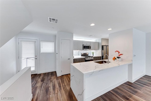 kitchen with sink, dark wood-type flooring, gray cabinets, stainless steel appliances, and kitchen peninsula